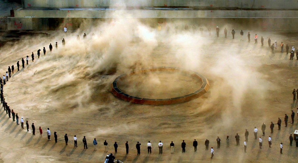 “Silence and Dust, 9/11 Memorial, 2002.” Rescue workers formed a circle on ground zero for a minute of silence in observance of the anniversary of the World Trade Center attacks.  A strong wind blew dust around the circle. © James Estrin/The New York Times
